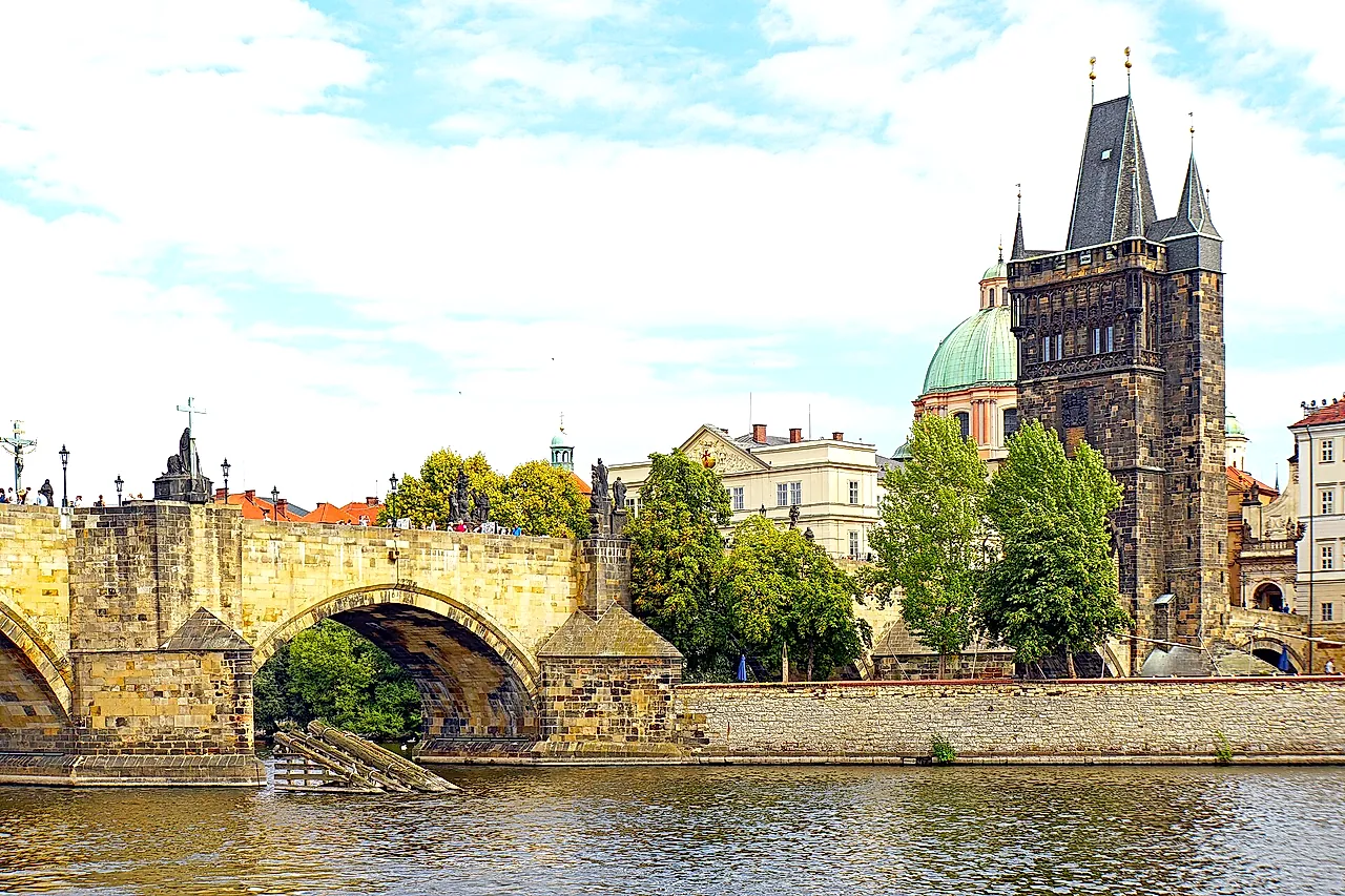 Charles Bridge over the Vltava, with its stone arches and statues along the parapet, and the Old Town Bridge Tower rising on the right under a blue sky.