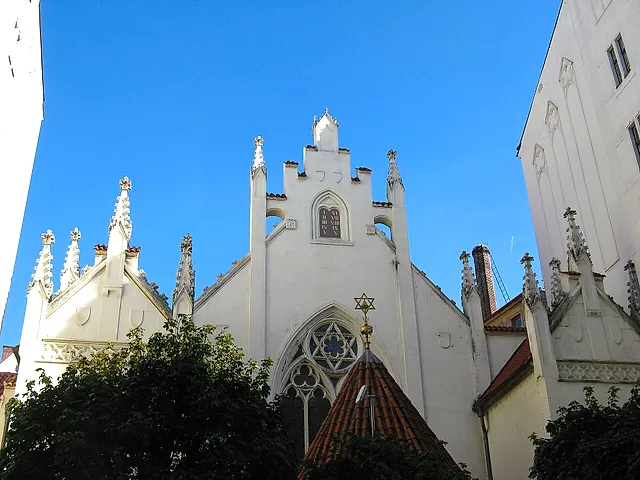 Facade of the Maisel Synagogue in Prague, a white Neo-Gothic building with pointed pinnacles and a stepped gable, framed by blue sky and tall neighbouring walls.