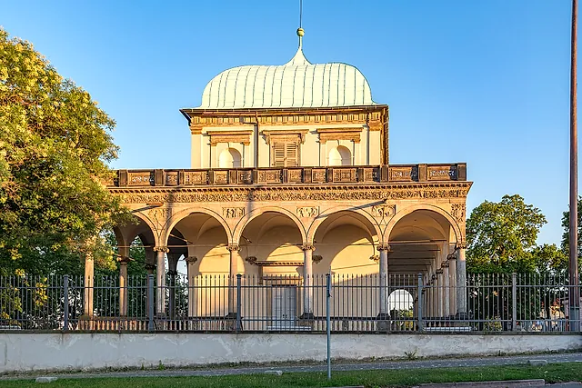 The Royal Summer Palace in the Prague Castle gardens, a Renaissance pavilion with a green copper dome, an arcaded loggia and an iron railing, in warm evening light.