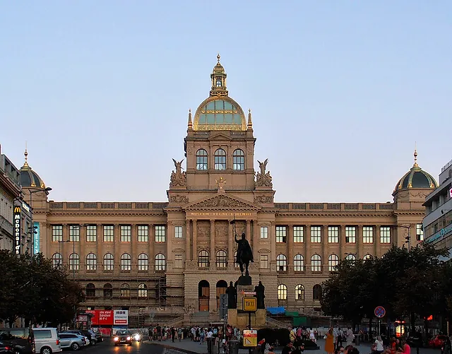 The National Museum at dusk, its central dome flanked by two smaller cupolas, sculpted statues on the facade and an equestrian statue standing in front.