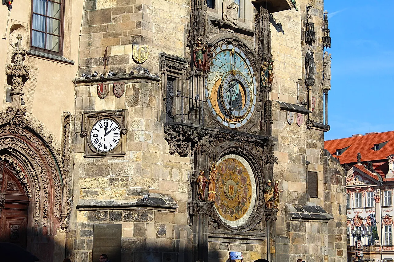 Close view of the Prague astronomical clock on the Old Town Hall tower, with its gold-and-blue astronomical dial, the Roman-numeral clock face and the carved figures around them.