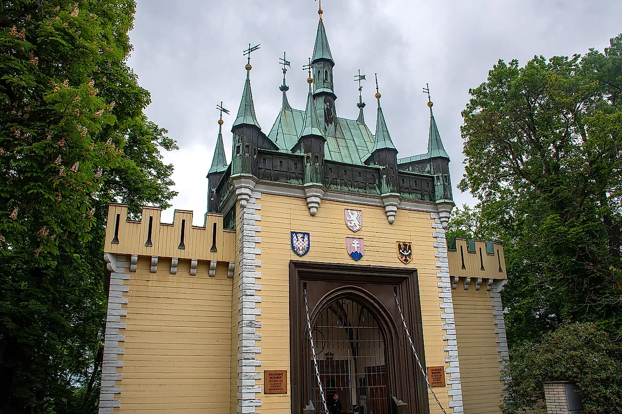 Entrance gate of the Mirror Maze on Petřín hill: a pale yellow turreted building with green copper roofs, a wooden door and heraldic shields above the arch.