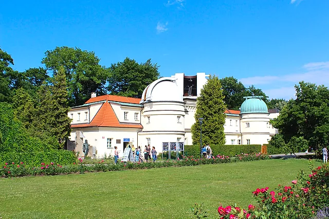 The Štefánik Observatory on Petřín hill: a white building with a round dome and a green-roofed tower, set on a lawn with red roses and a few visitors.