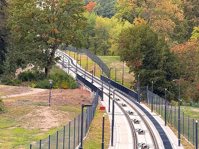 Funicular track climbing a wooded slope on Petřín hill in autumn, with a metal fence along the line, lamp posts beside the path and no car in view.