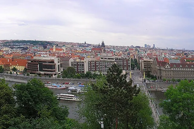 Wide panorama of Prague from Letná hill, with the red-roofed city, the river winding between bridges and hills fading into a hazy horizon.