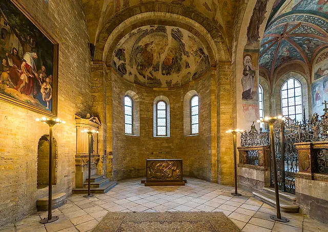 Interior of St George's Basilica at Prague Castle, with the medieval apse, faded frescoes in the vault, narrow arched windows and a metal chest with a relief in front of the apse.
