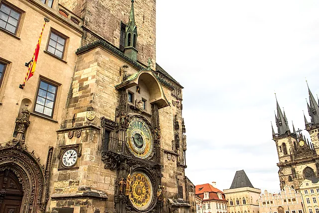 Astronomical clock on the Old Town Hall tower, seen from the side, with its blue astronomical dial and calendar dial below, and the spires of Týn Church beyond.