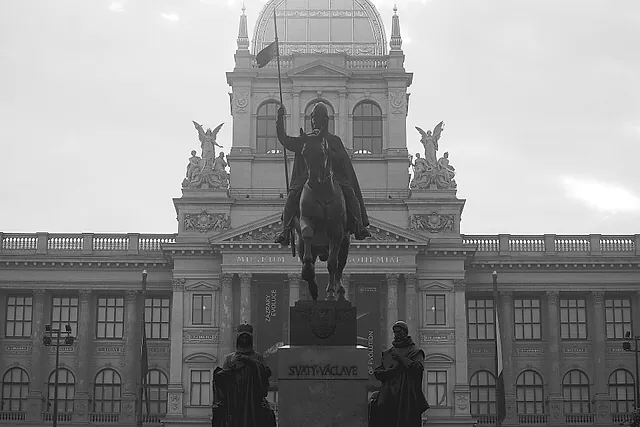 Black-and-white view of the National Museum in Prague, with its glazed dome, sculpted figures on the roofline and the equestrian monument of St Wenceslas in front, under a grey sky.